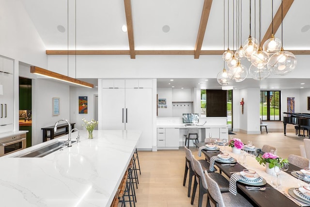 dining area with beamed ceiling, sink, a high ceiling, and light wood-type flooring