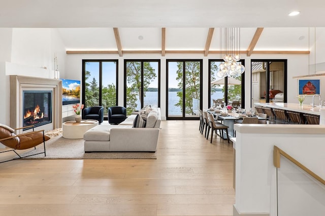 living room with an inviting chandelier, beam ceiling, light hardwood / wood-style flooring, and a water view