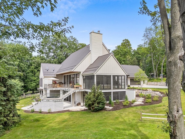 rear view of house featuring a patio, a deck, a sunroom, and a lawn