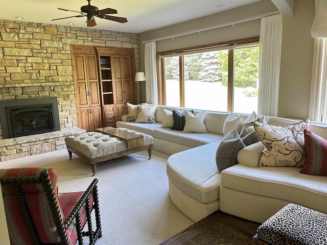 carpeted living room with a stone fireplace and ceiling fan