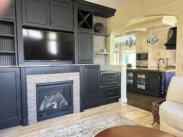 living room with a tile fireplace, crown molding, sink, light hardwood / wood-style flooring, and a notable chandelier