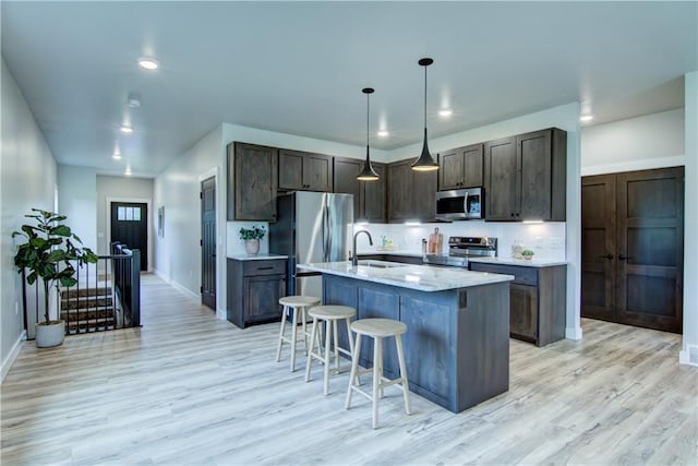 kitchen with appliances with stainless steel finishes, sink, pendant lighting, a center island with sink, and light hardwood / wood-style flooring