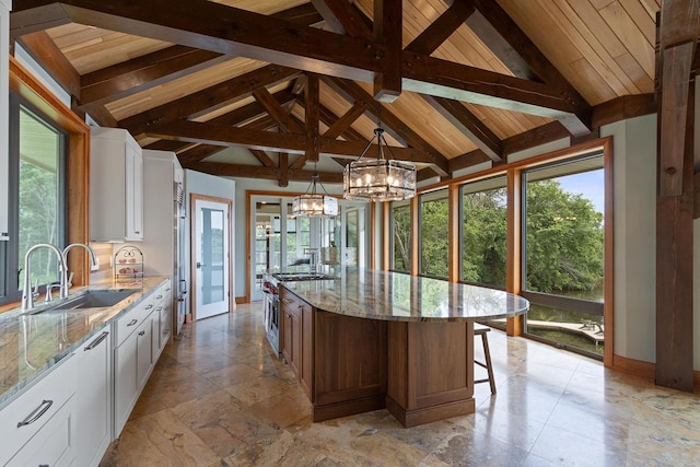 kitchen featuring light stone countertops, sink, beam ceiling, white cabinets, and a center island