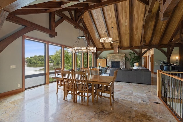 dining room featuring beam ceiling, a water view, high vaulted ceiling, wooden ceiling, and a stone fireplace