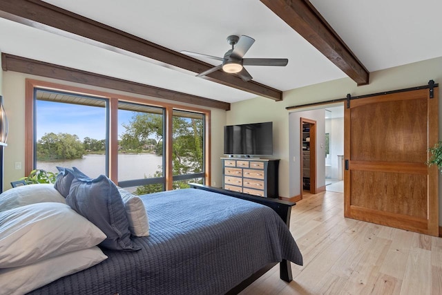 bedroom with a barn door, ceiling fan, beamed ceiling, and light hardwood / wood-style floors