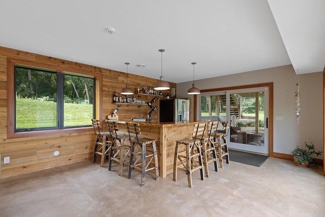 kitchen with a breakfast bar, hanging light fixtures, stainless steel refrigerator with ice dispenser, wooden walls, and kitchen peninsula