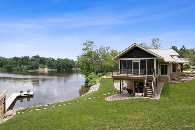 rear view of house featuring a sunroom, a water view, and a lawn