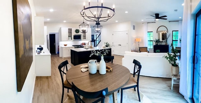 dining space with light wood-type flooring, ceiling fan with notable chandelier, and sink