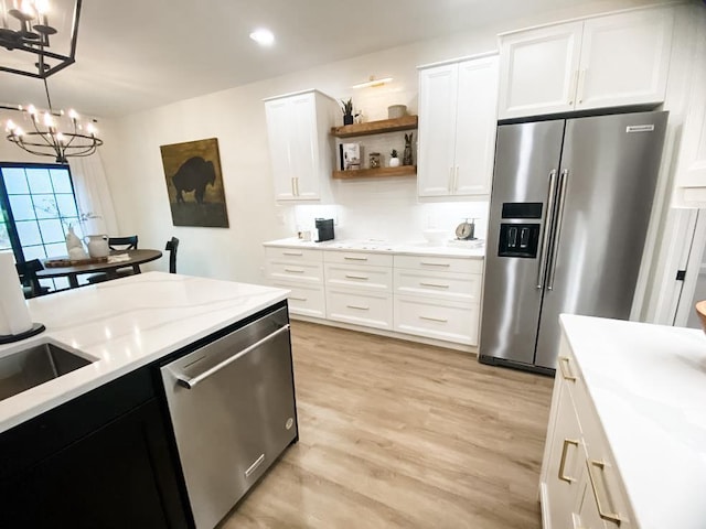 kitchen with hanging light fixtures, stainless steel appliances, an inviting chandelier, light hardwood / wood-style flooring, and white cabinets