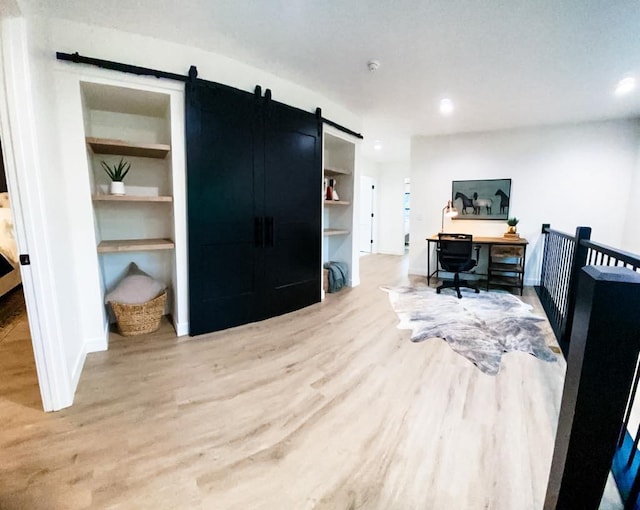 home office with built in shelves, a barn door, and light hardwood / wood-style floors