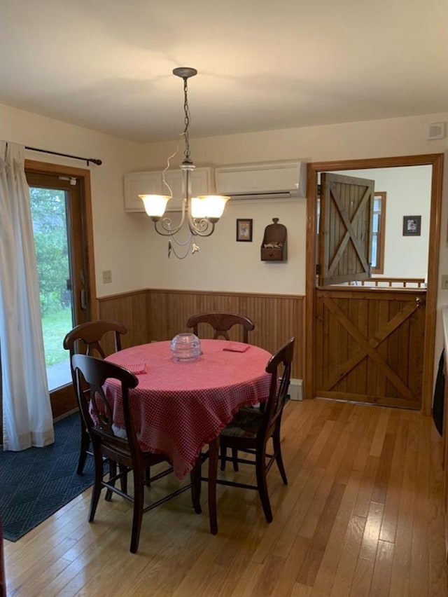 dining space featuring a wall unit AC, wooden walls, an inviting chandelier, and hardwood / wood-style flooring