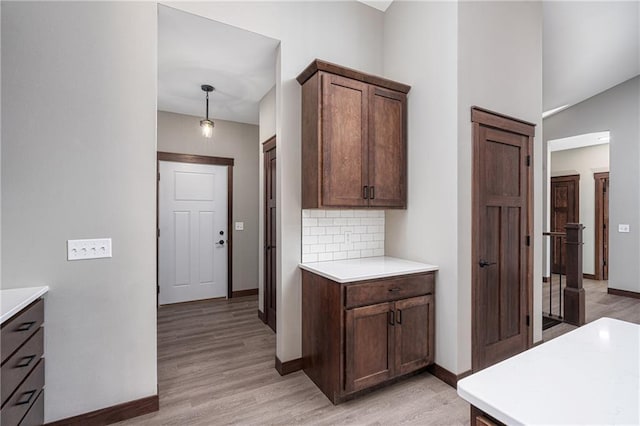 kitchen featuring light wood-type flooring, decorative light fixtures, dark brown cabinetry, and backsplash