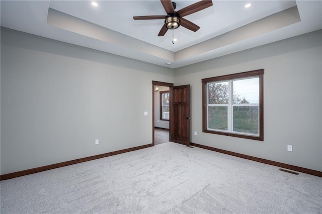 empty room featuring a tray ceiling, ceiling fan, and carpet