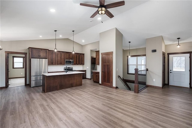 kitchen with appliances with stainless steel finishes, backsplash, wood-type flooring, decorative light fixtures, and a center island with sink