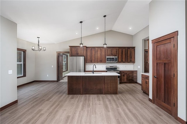 kitchen with lofted ceiling, a kitchen island with sink, hanging light fixtures, light hardwood / wood-style flooring, and stainless steel appliances