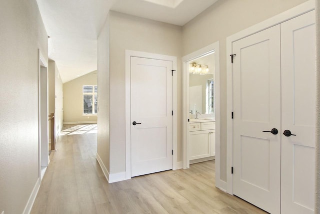 hallway with lofted ceiling, light wood-type flooring, and sink