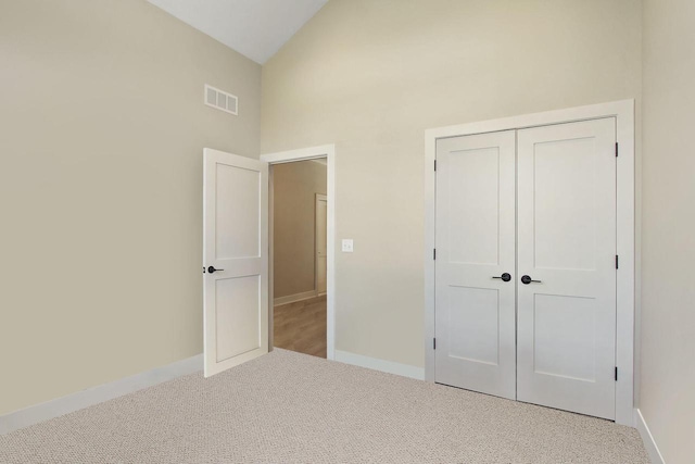 unfurnished bedroom featuring light colored carpet, high vaulted ceiling, and a closet