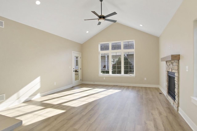 unfurnished living room with ceiling fan, a stone fireplace, high vaulted ceiling, and light hardwood / wood-style flooring