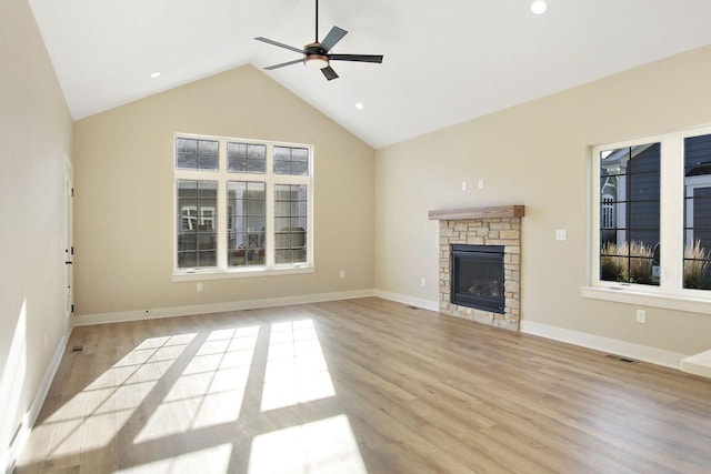 unfurnished living room with high vaulted ceiling, light hardwood / wood-style floors, a stone fireplace, and ceiling fan