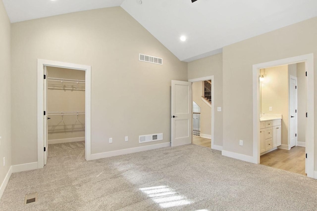 unfurnished bedroom with light carpet, high vaulted ceiling, ensuite bathroom, a walk in closet, and a closet