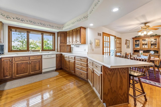 kitchen with kitchen peninsula, a kitchen breakfast bar, light wood-type flooring, and white dishwasher