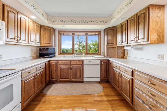 kitchen with white appliances, light hardwood / wood-style floors, a tray ceiling, and sink