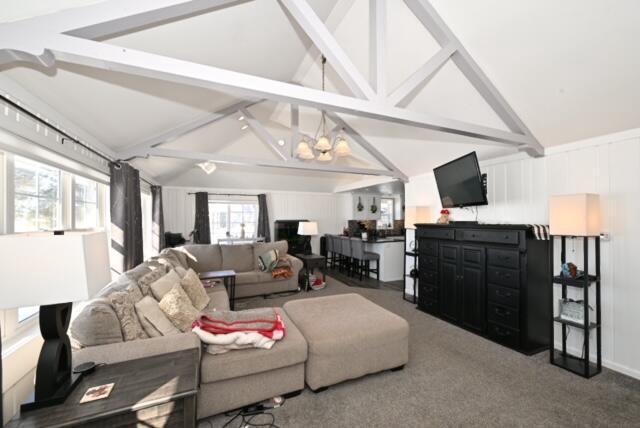 carpeted living room with vaulted ceiling with beams and a chandelier