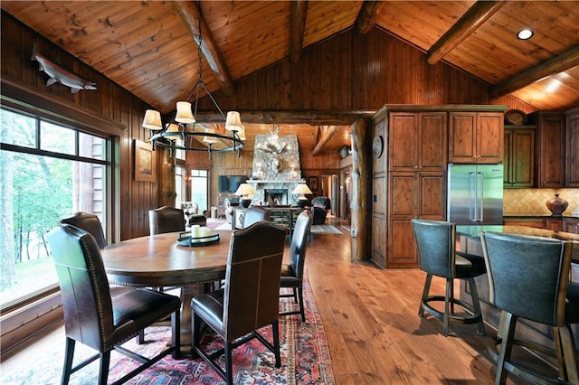 dining space with wooden ceiling, a stone fireplace, lofted ceiling with beams, a chandelier, and light wood-type flooring