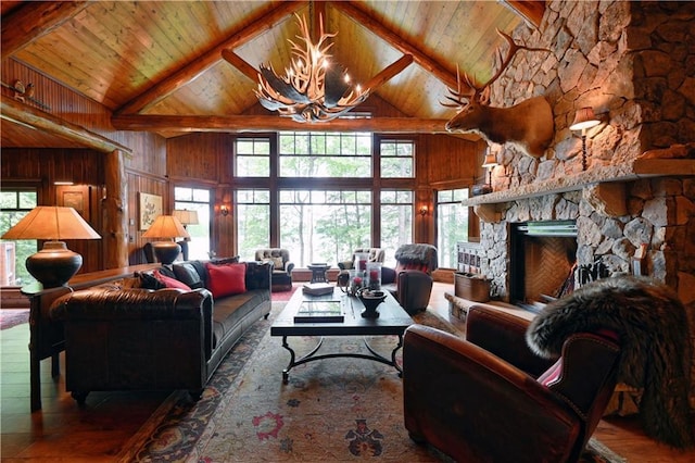 living room featuring a stone fireplace, beamed ceiling, high vaulted ceiling, wood walls, and a chandelier