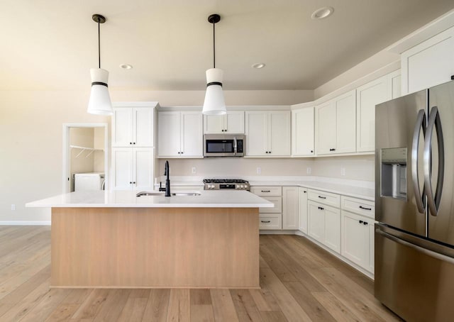 kitchen with stainless steel appliances, a kitchen island with sink, sink, white cabinetry, and hanging light fixtures