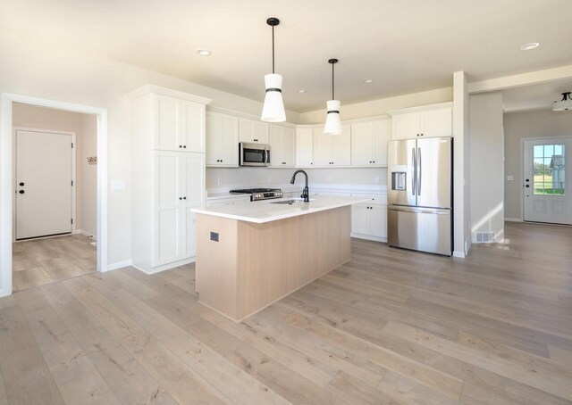 kitchen with white cabinets, sink, stainless steel appliances, and an island with sink