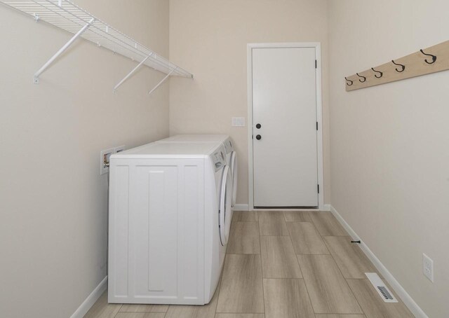 laundry area featuring washing machine and clothes dryer and light hardwood / wood-style floors