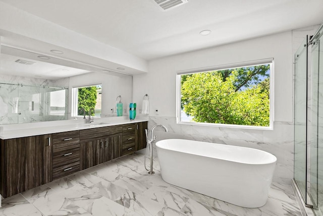 bathroom featuring plus walk in shower, vanity, a healthy amount of sunlight, and tile walls