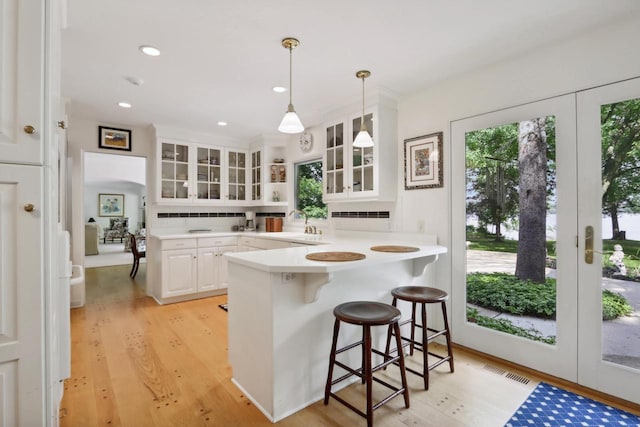 kitchen featuring kitchen peninsula, a kitchen breakfast bar, tasteful backsplash, white cabinetry, and hanging light fixtures