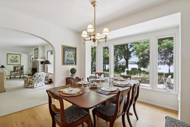 dining area featuring a brick fireplace, a notable chandelier, and light wood-type flooring