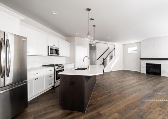 kitchen featuring white cabinetry, sink, stainless steel appliances, decorative light fixtures, and a center island with sink