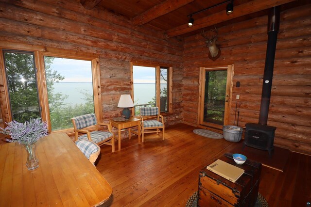 sitting room with beamed ceiling, wood-type flooring, rustic walls, and a wealth of natural light