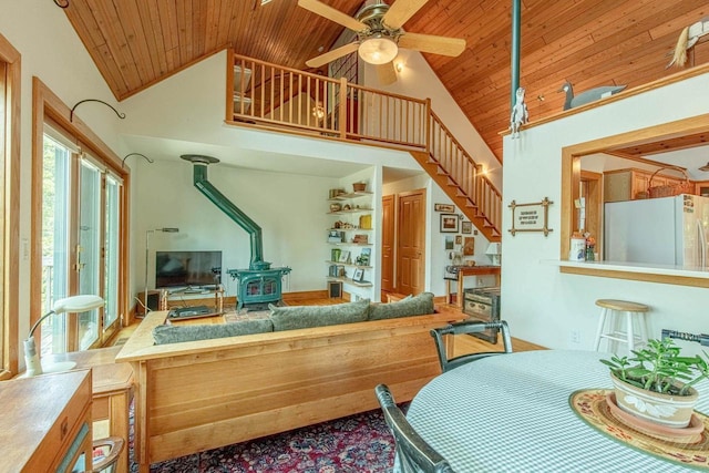 interior space with wood ceiling, high vaulted ceiling, ceiling fan, and a wood stove