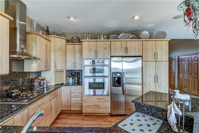 kitchen with wall chimney exhaust hood, light hardwood / wood-style floors, light brown cabinetry, and appliances with stainless steel finishes