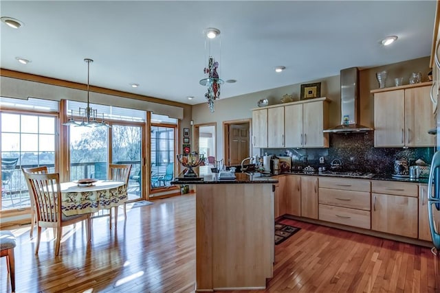 kitchen featuring pendant lighting, light brown cabinets, wall chimney range hood, and backsplash