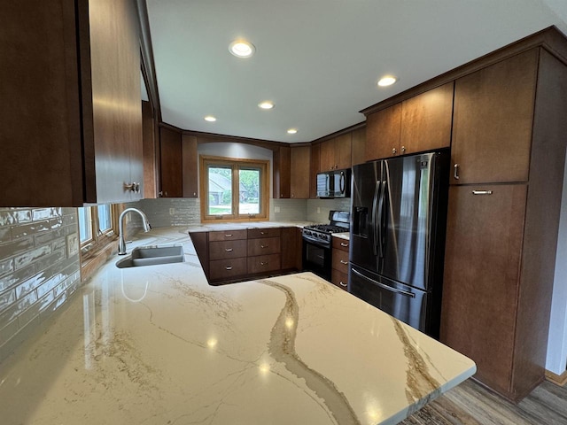 kitchen with kitchen peninsula, light stone counters, gas stove, sink, and stainless steel fridge with ice dispenser