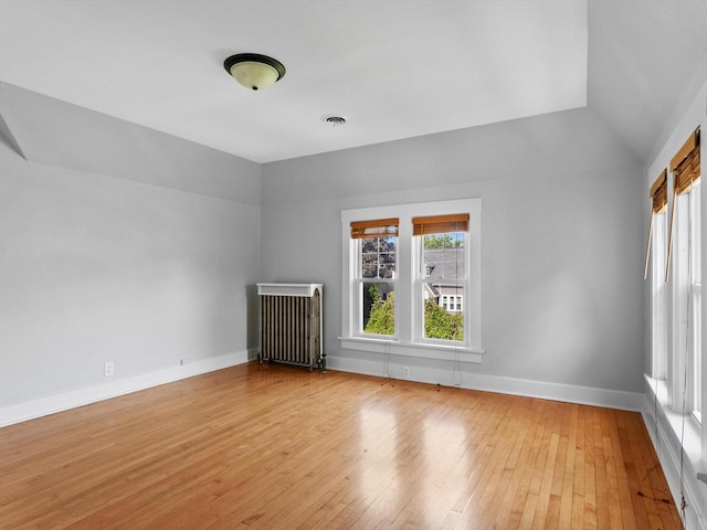 spare room with lofted ceiling, radiator heating unit, and light hardwood / wood-style flooring