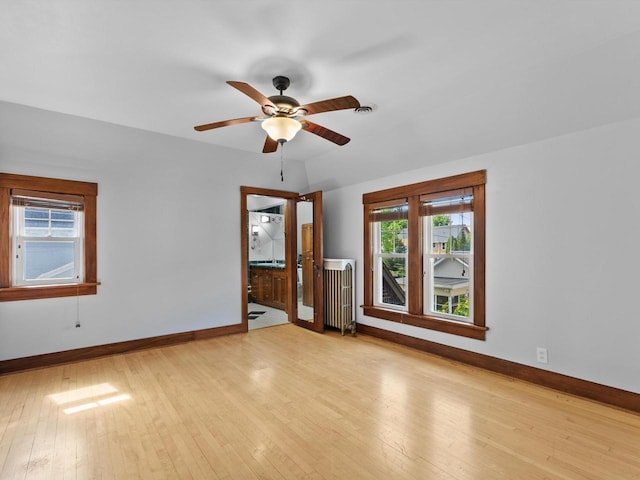 unfurnished room with radiator heating unit, light wood-type flooring, and ceiling fan