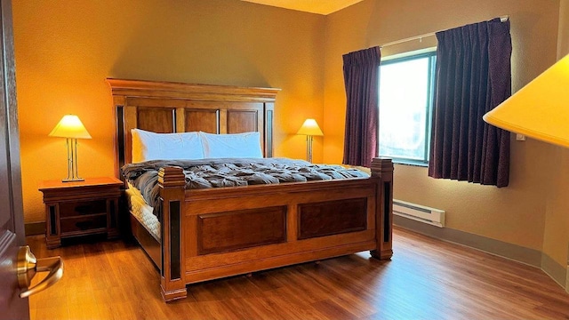 bedroom featuring hardwood / wood-style floors and a baseboard heating unit