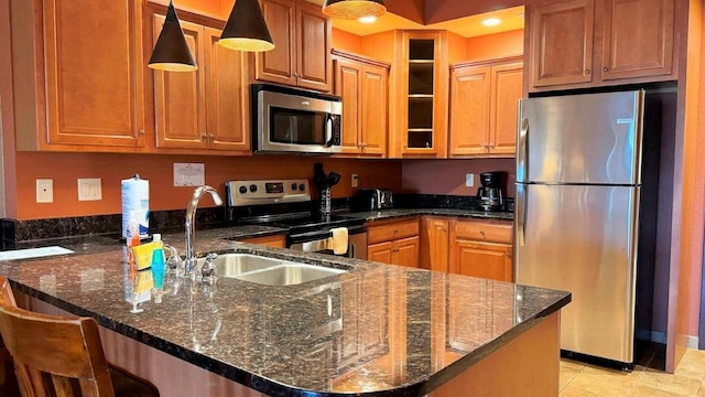 kitchen with appliances with stainless steel finishes, a kitchen breakfast bar, dark stone counters, sink, and pendant lighting