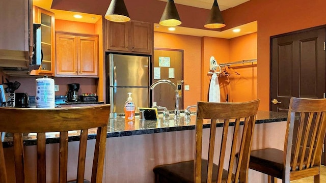 kitchen featuring stainless steel fridge, decorative light fixtures, dark stone counters, and sink