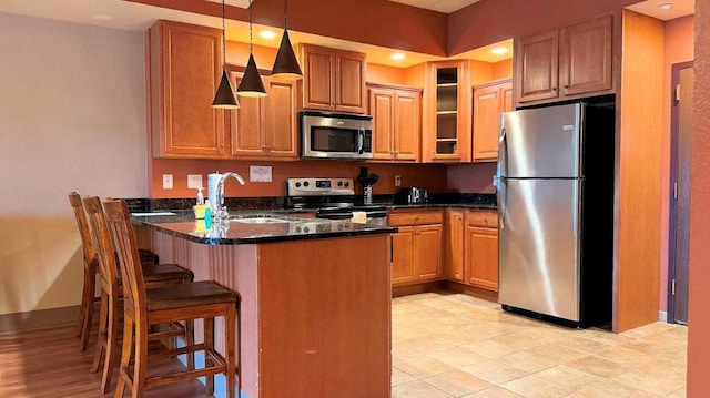 kitchen featuring sink, stainless steel appliances, kitchen peninsula, dark stone counters, and a breakfast bar