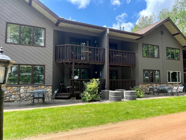 back of property featuring central AC unit, a patio area, a balcony, and a yard