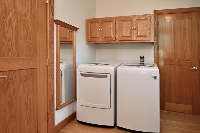 clothes washing area featuring baseboards, cabinet space, light wood-style flooring, and washer and clothes dryer