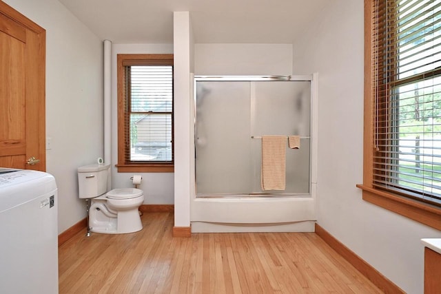 bathroom featuring washer / clothes dryer, toilet, a healthy amount of sunlight, and wood finished floors